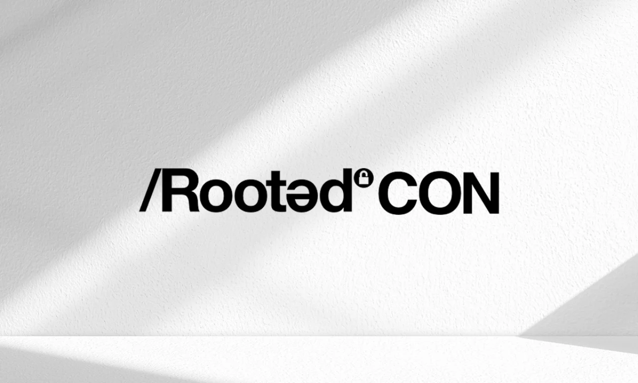 Black RootedCON logo with stylized text and small padlock symbol on a white textured wall with diagonal shadows.