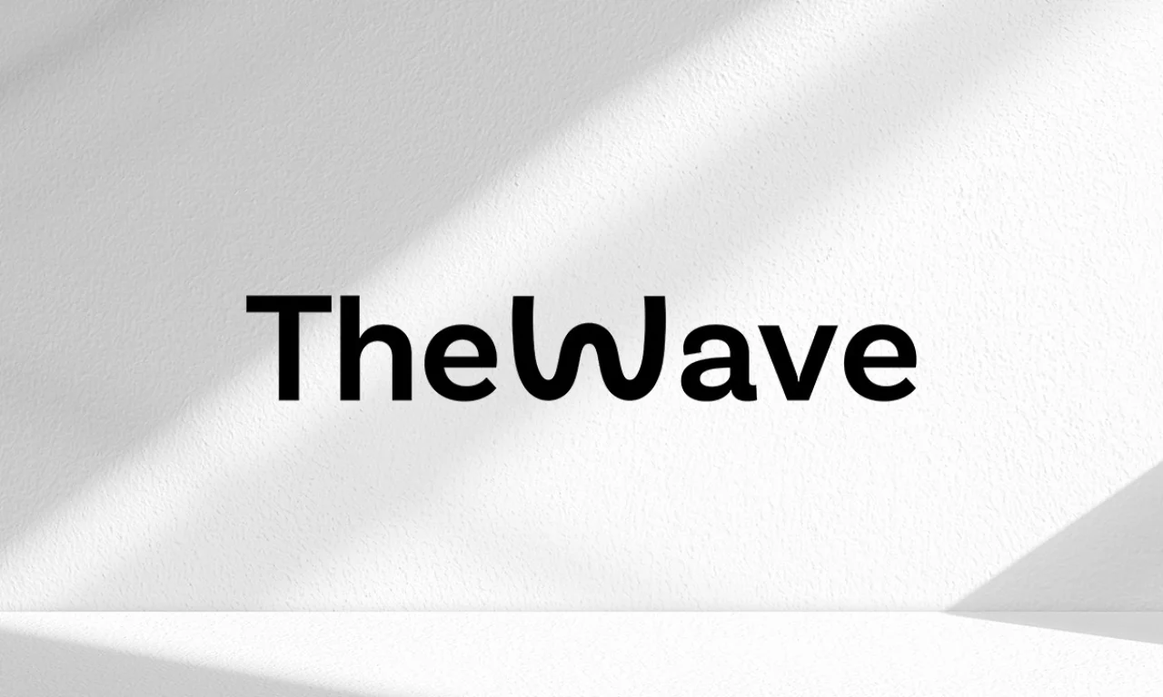 Black The Wave logo with stylized flowing typography centered on a white textured wall with soft diagonal lighting.
