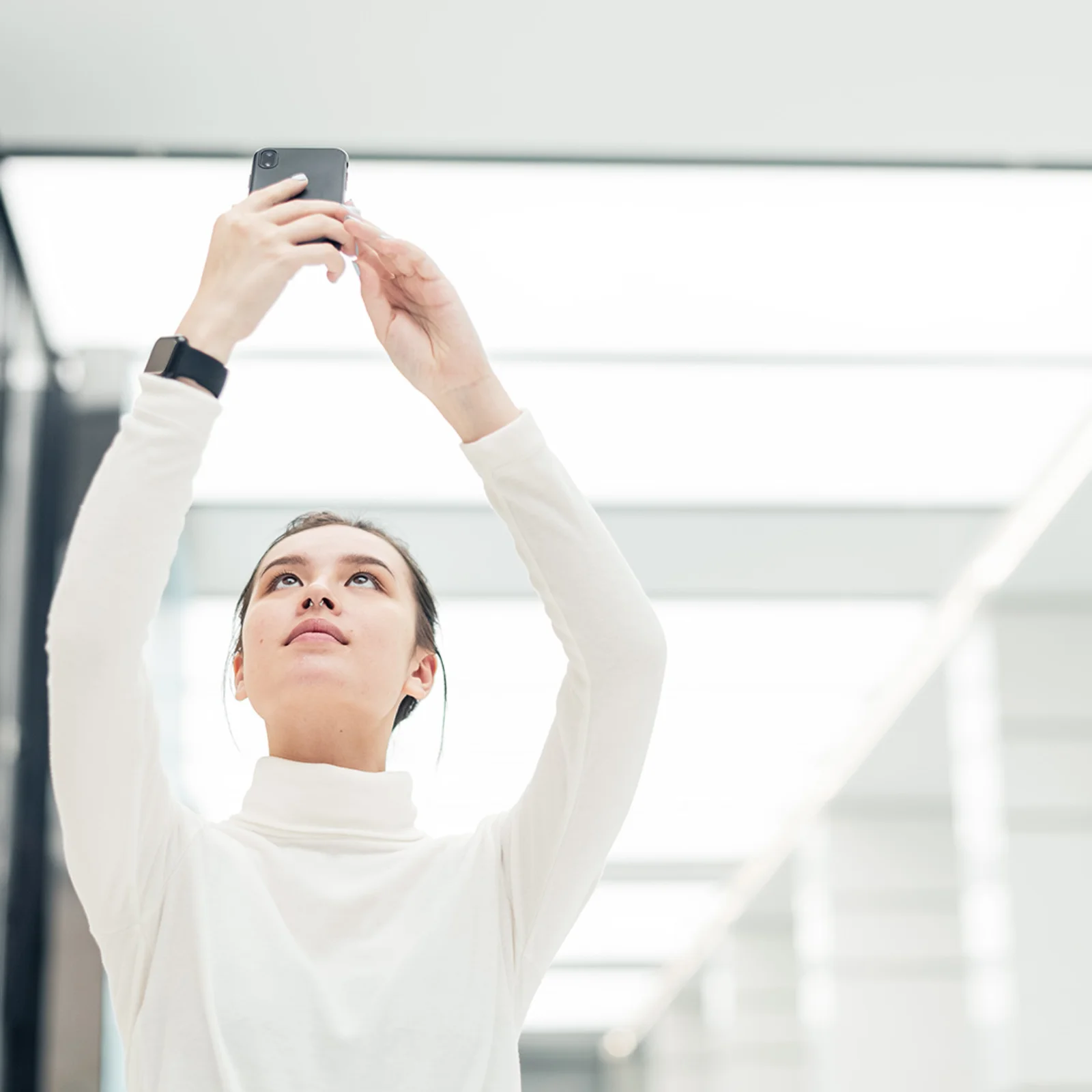 Capturing Innovation in a Digital World Person in a bright modern space holding up a smartphone, symbolizing technology, creativity, and digital connectivity.