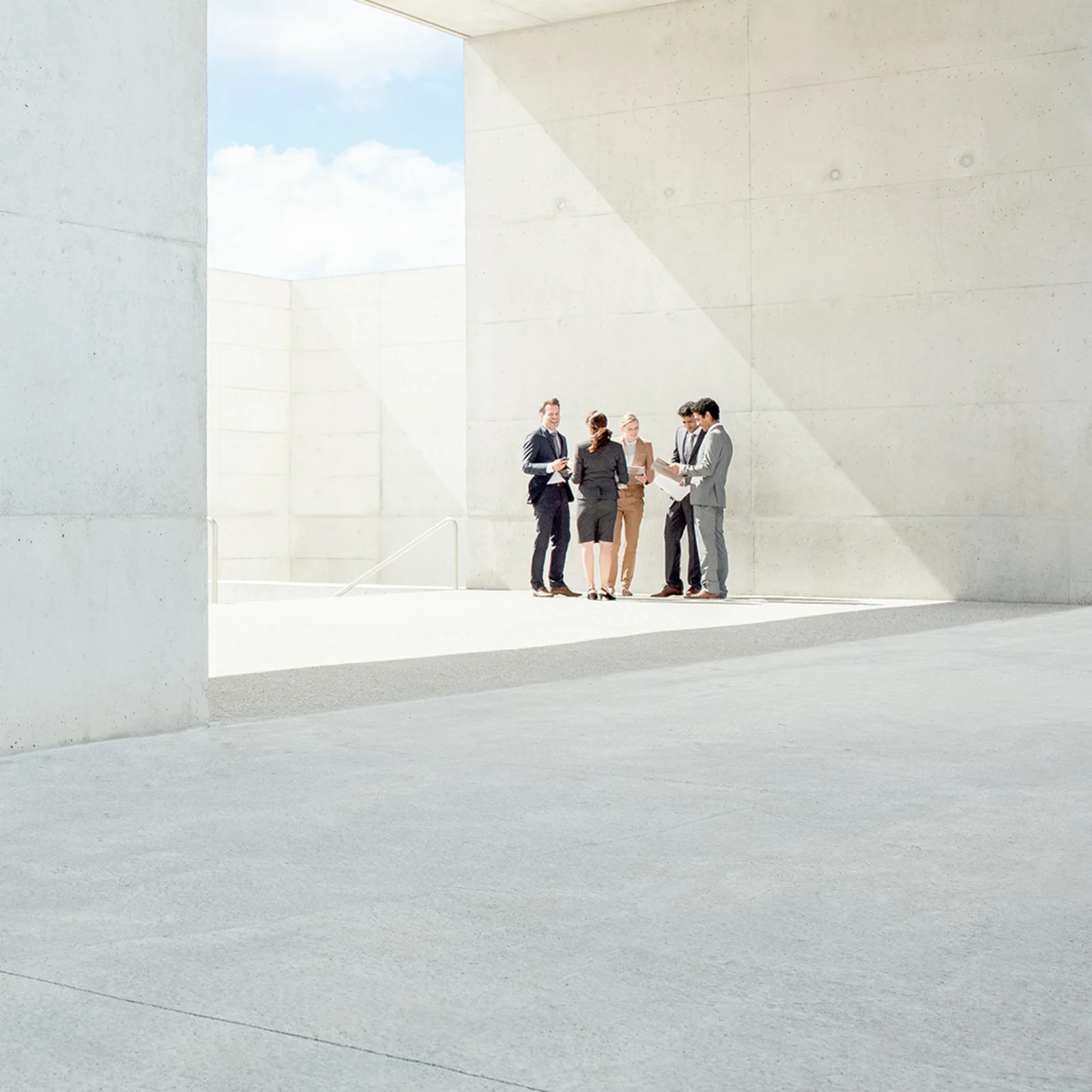 GFT - Agile and Devops Solutions 02 Group of business professionals discussing work outside a modern concrete building under bright daylight.