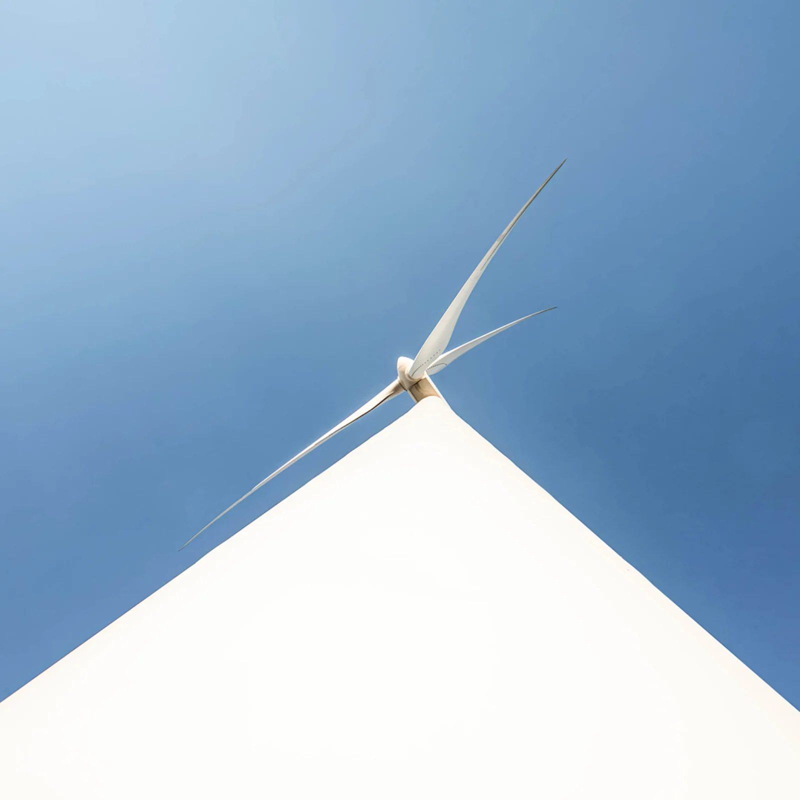 Upward view of a modern white wind turbine set against a clear blue sky, symbolizing renewable energy and clean technology.