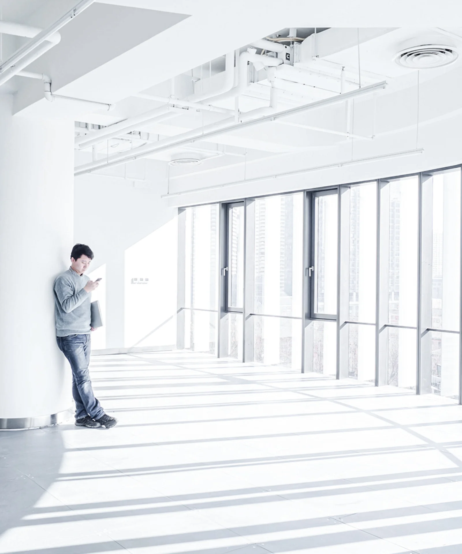 Person standing in a bright, minimalist office with large windows, using a tablet to explore digital solutions and innovation.