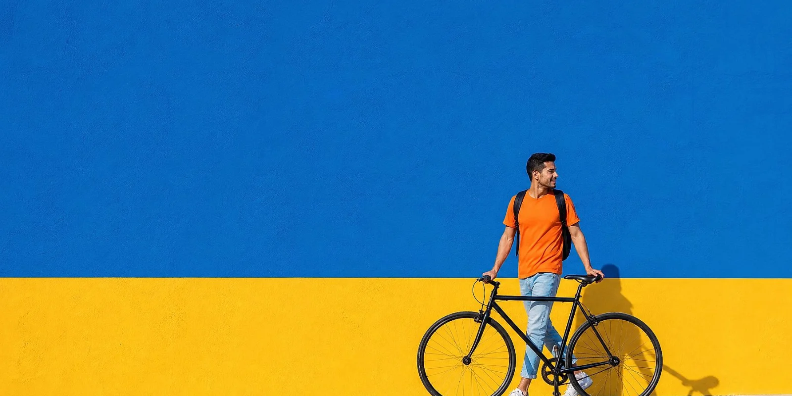 Person walking beside a bicycle against a minimalist yellow wall, representing eco-friendly urban mobility and modern living.