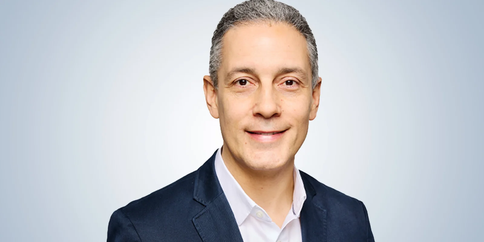 Professional portrait of a business leader in a dark suit and light shirt, smiling confidently against a light gradient background.
