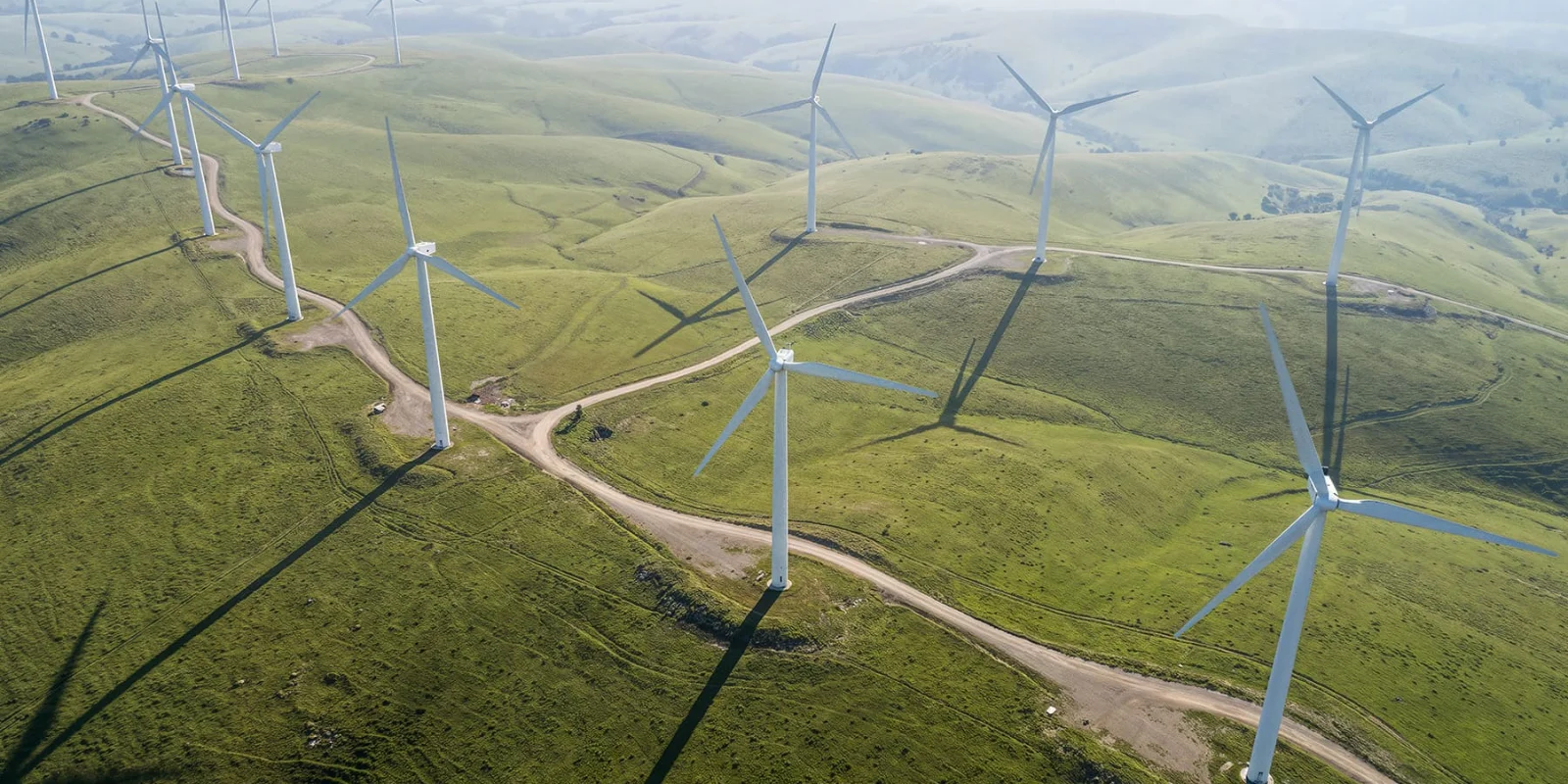 Aerial view of multiple wind turbines across rolling green hills, generating renewable energy in a large-scale wind farm landscape.