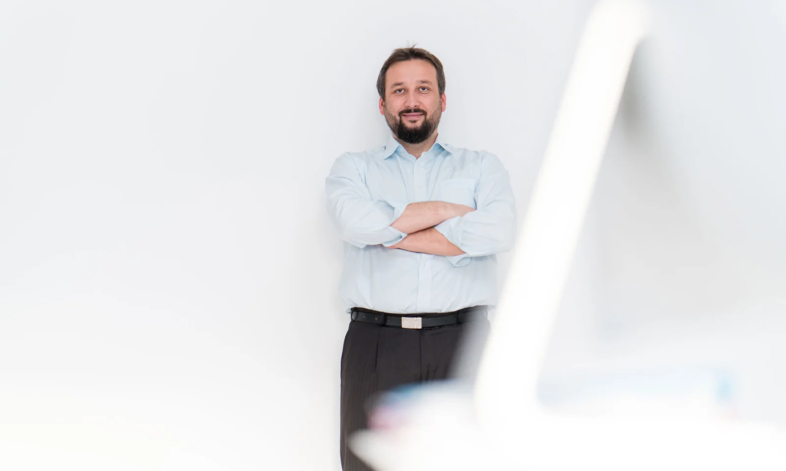 Un experto en tecnología de GFT, seguro de sí mismo, de pie, con los brazos cruzados, vestido con una camisa azul claro y sobre un fondo blanco. La imagen transmite profesionalidad e innovación. GettyImages-1071771838.jpg