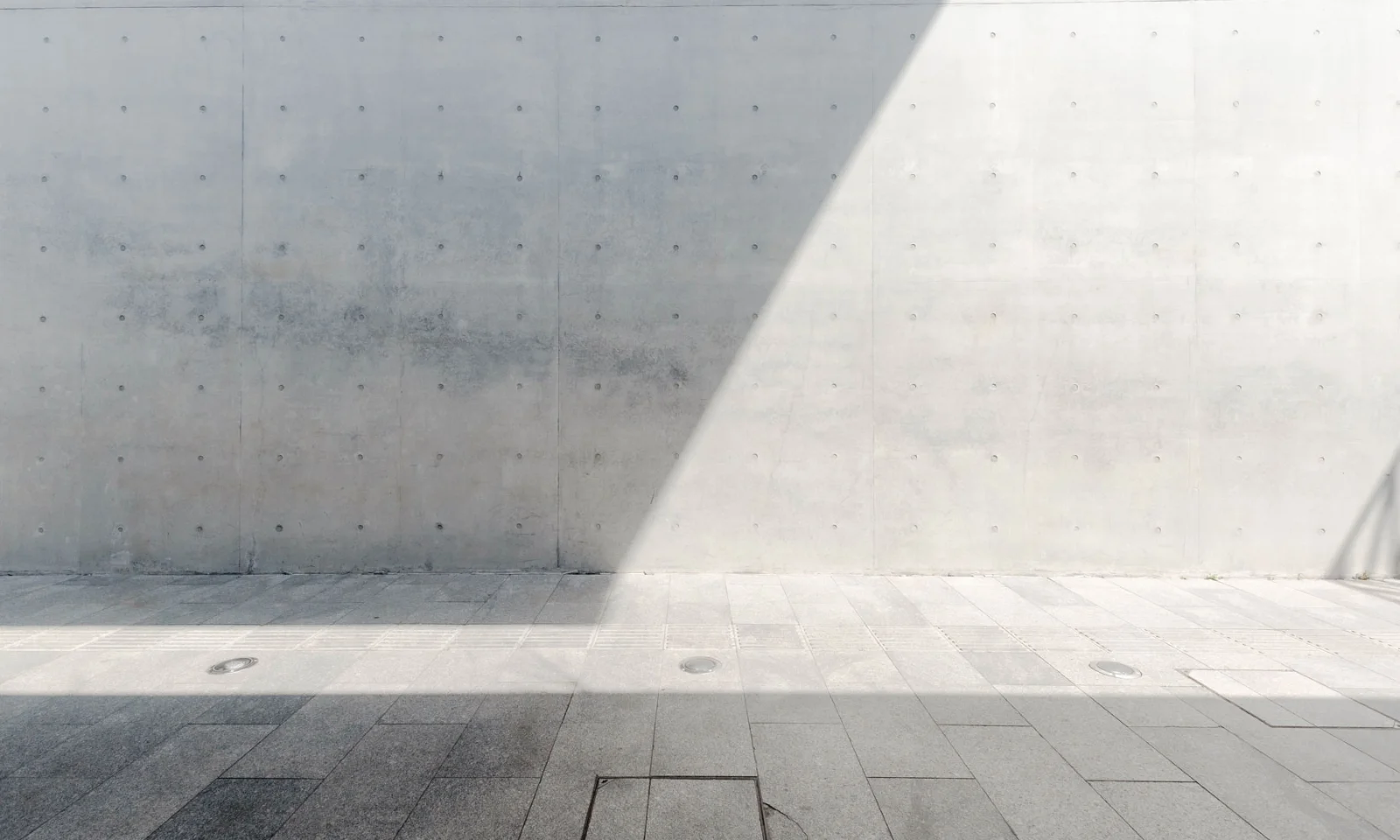 Minimalist concrete wall and tiled floor with a sharp diagonal shadow cast by sunlight, creating a modern architectural composition