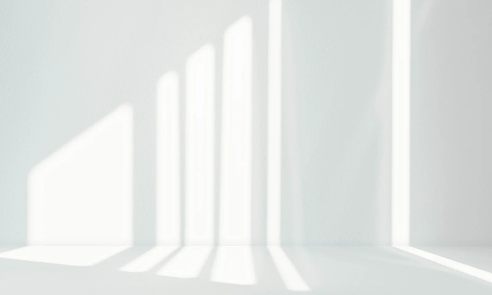 Soft vertical beams of natural light casting clean geometric shadows on a white textured wall and surface.