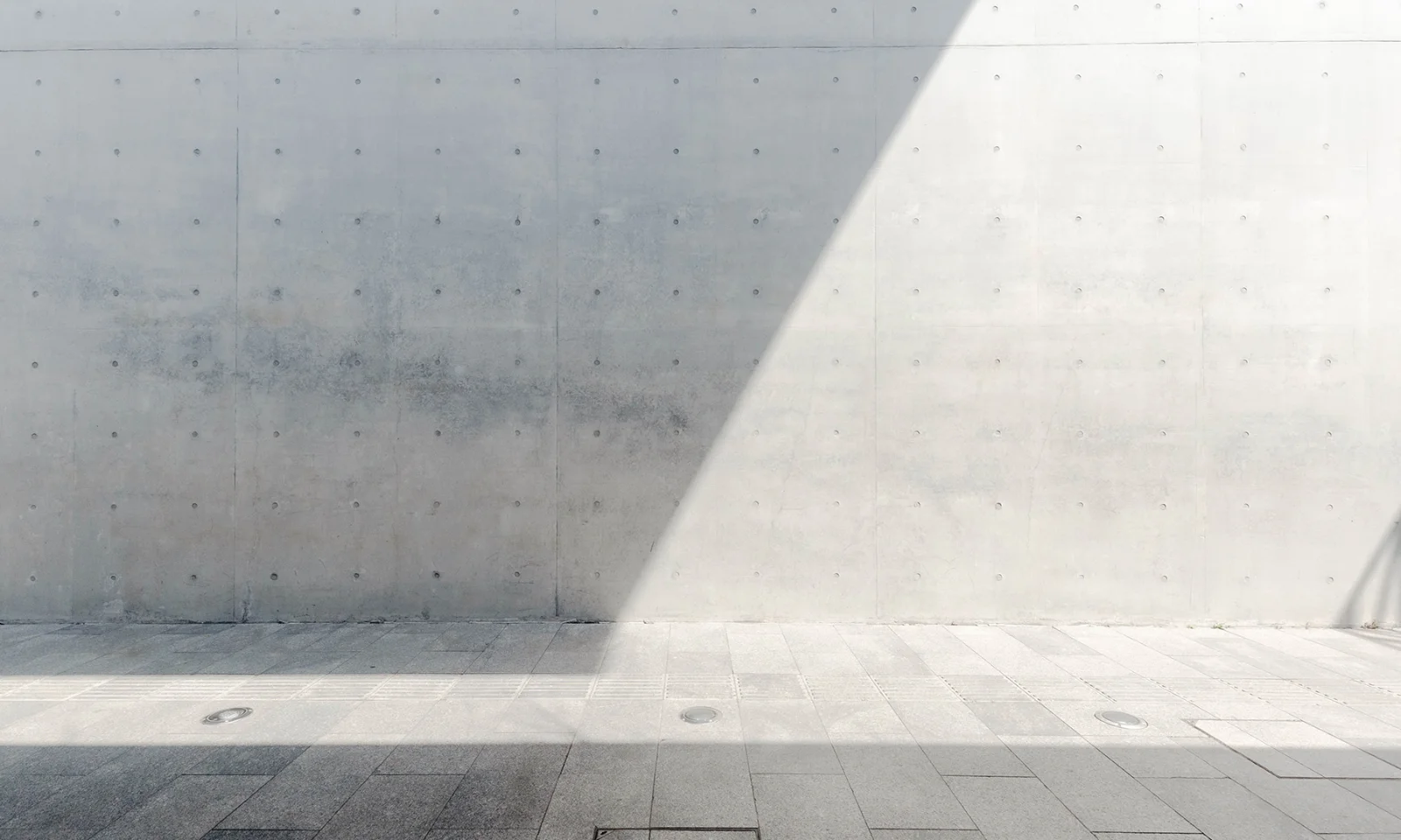 Minimalist Concrete Wall with Geometric Shadow Smooth concrete wall with a diagonal shadow cast across its surface, creating a minimalist and modern architectural composition.