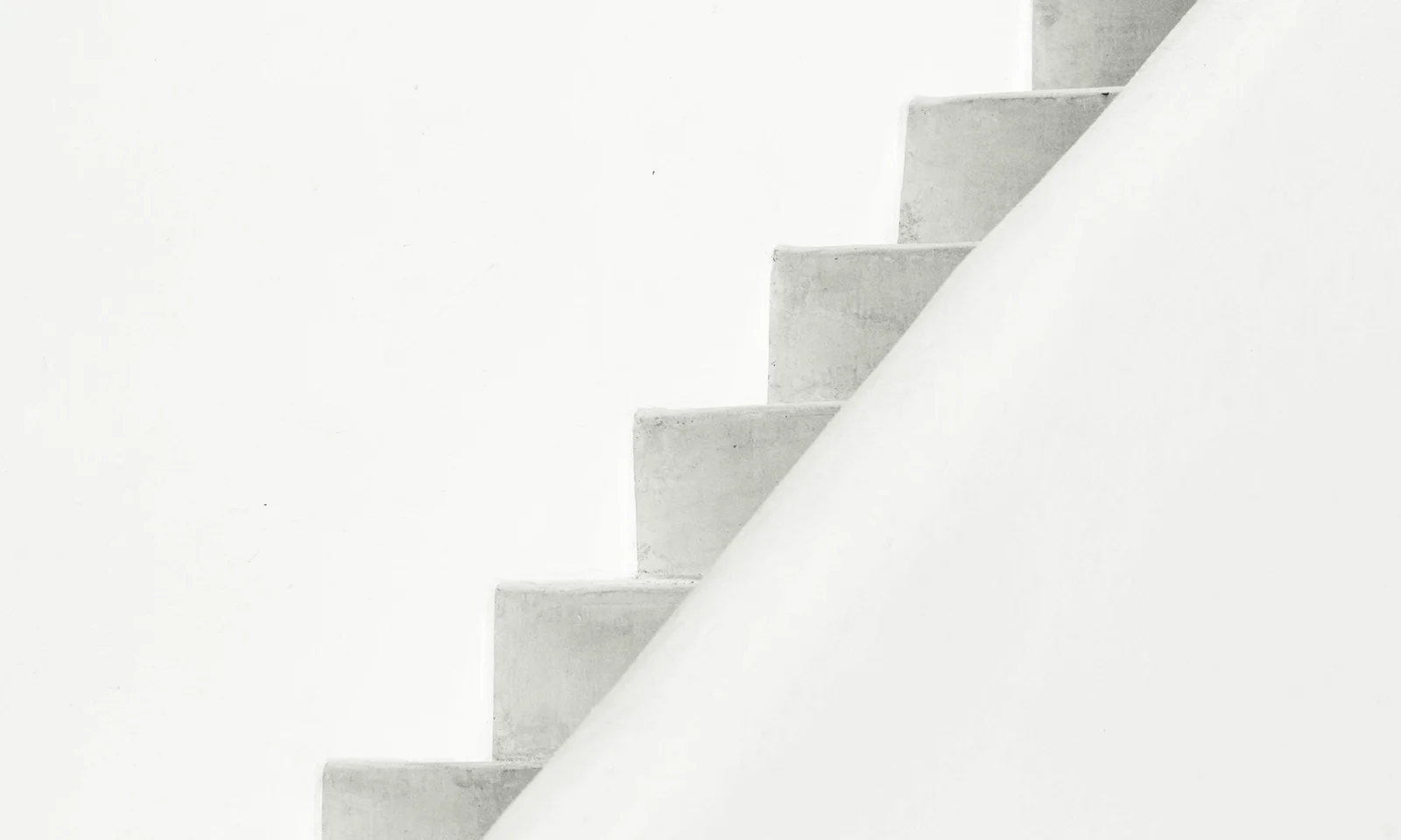 Diagonal view of a simple concrete staircase set against a bright white wall in a minimalist architectural setting.