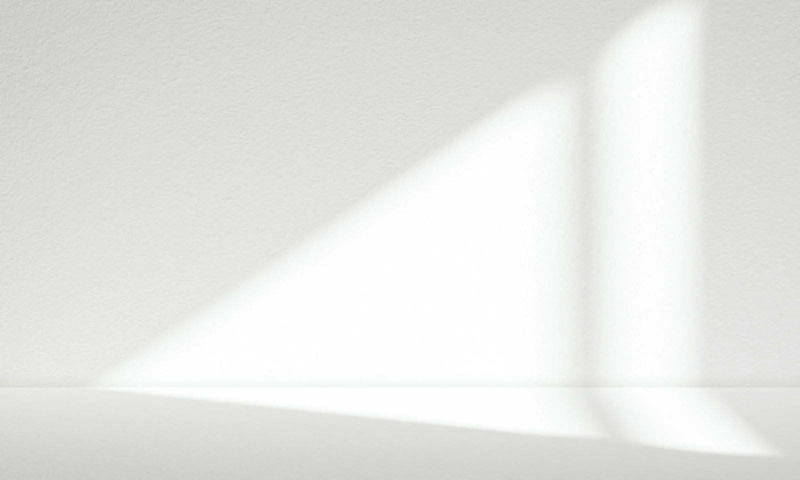 Abstract Light and Shadow on White Surface Sunlight forming geometric shapes and soft shadows on a white textured wall, creating a clean, minimalist visual.