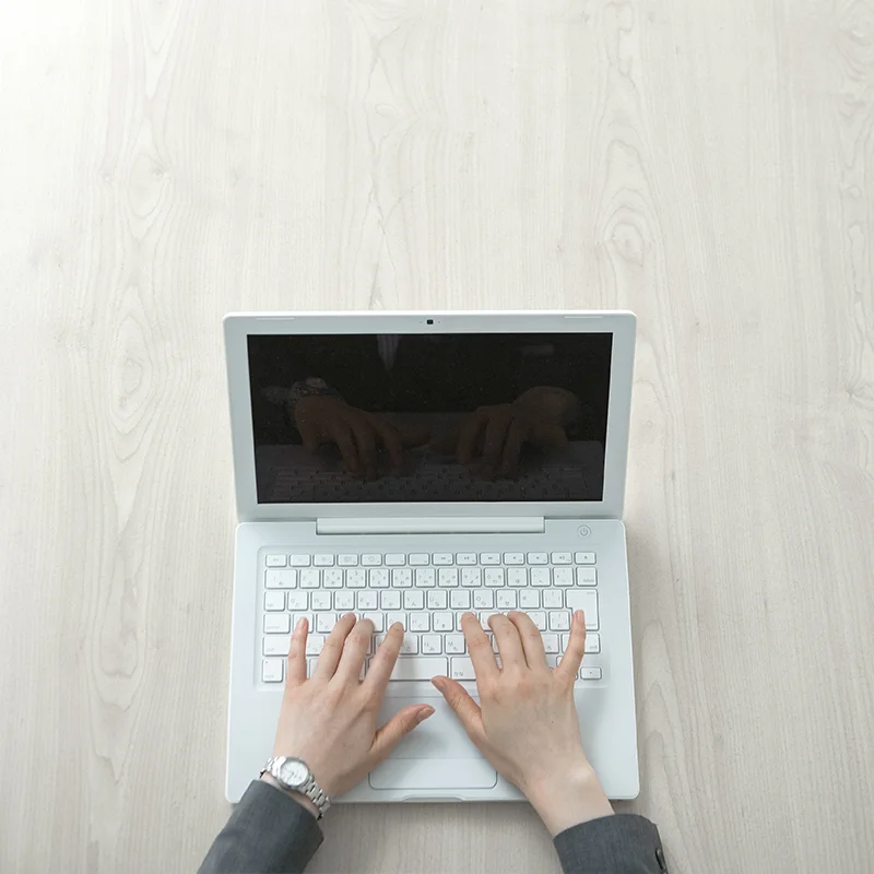 Hands typing on a white laptop on a light wooden desk, symbolizing digital collaboration and innovation