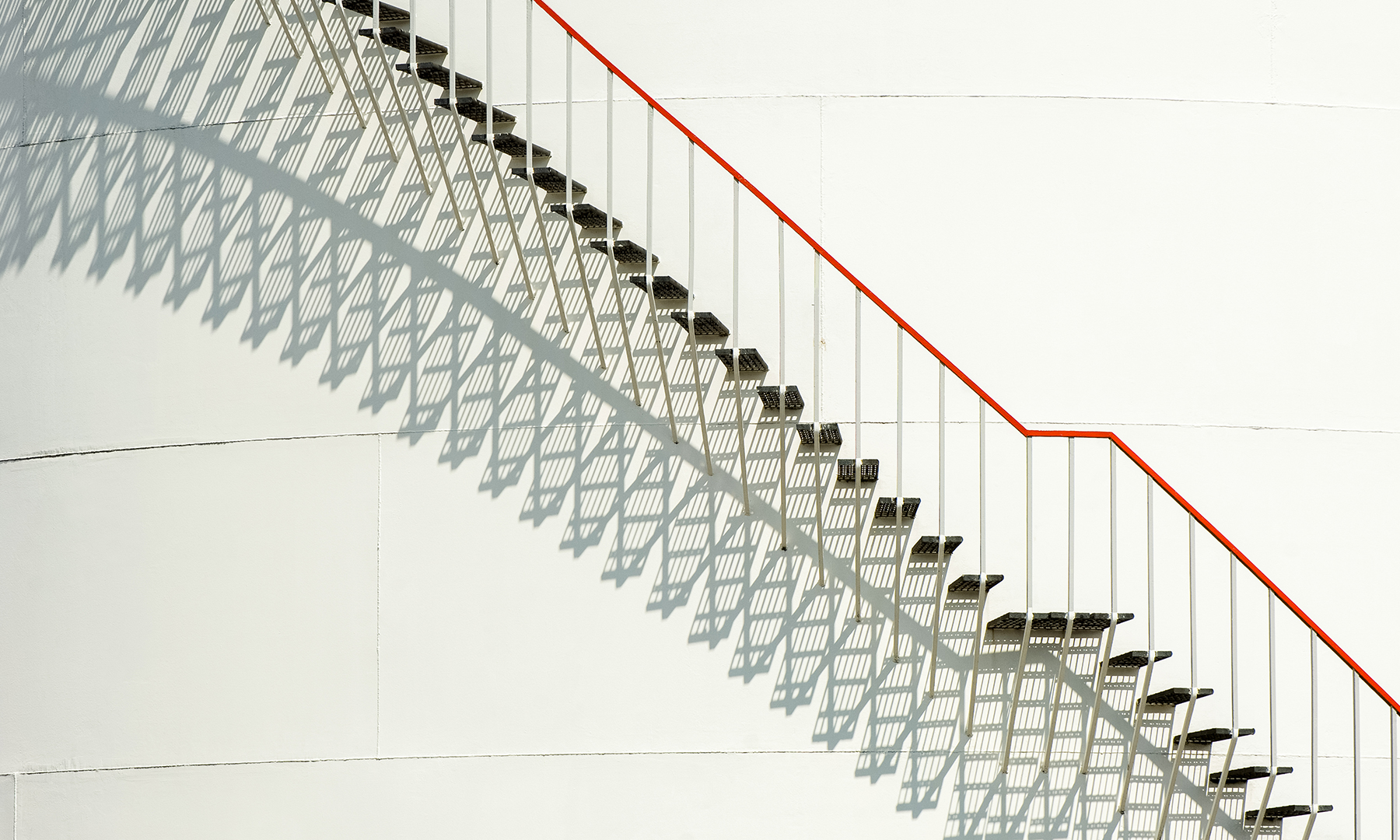 Modern staircase with geometric shadows and a red handrail, symbolizing progress, precision, and structured innovation.