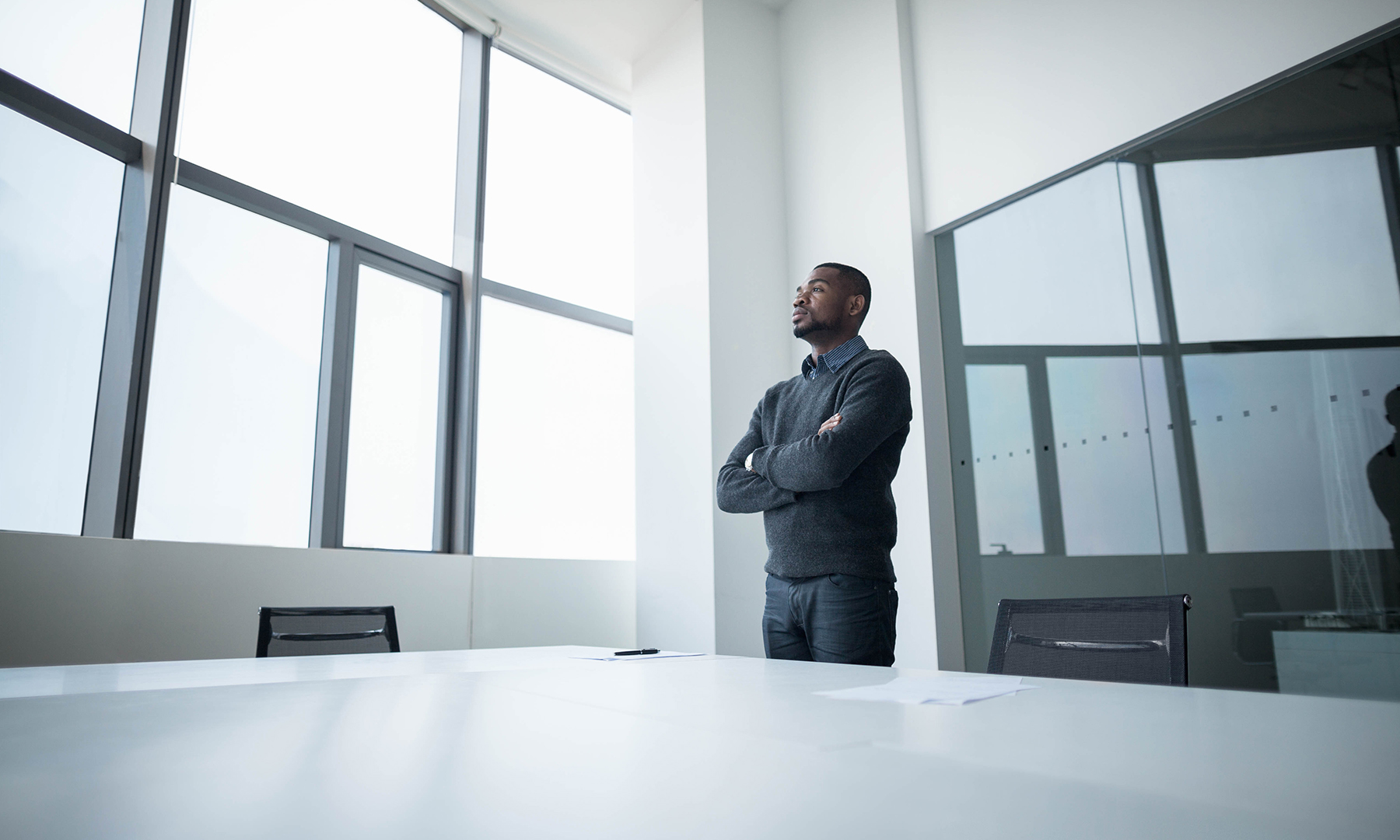 Business professional standing in a modern office, looking thoughtfully out the window, symbolizing leadership and forward-thinking.