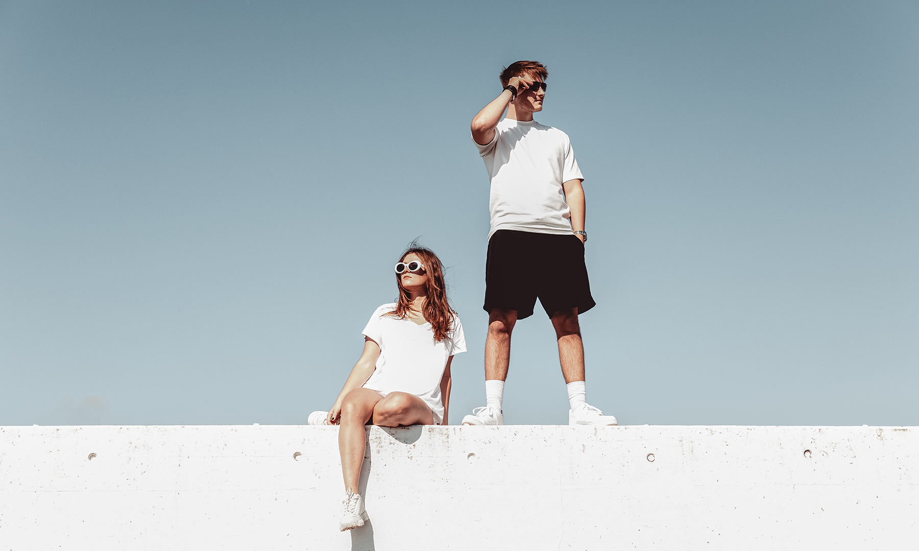 Two people in minimalist white outfits under a clear sky, symbolizing forward vision and innovation.