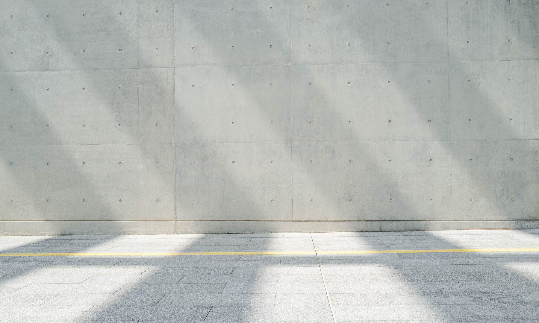GFT Solution: Automatyzacja Procesow Modern concrete facade with evenly spaced anchor points and subtle vertical shadows falling across a light grey paved walkway with a yellow line
