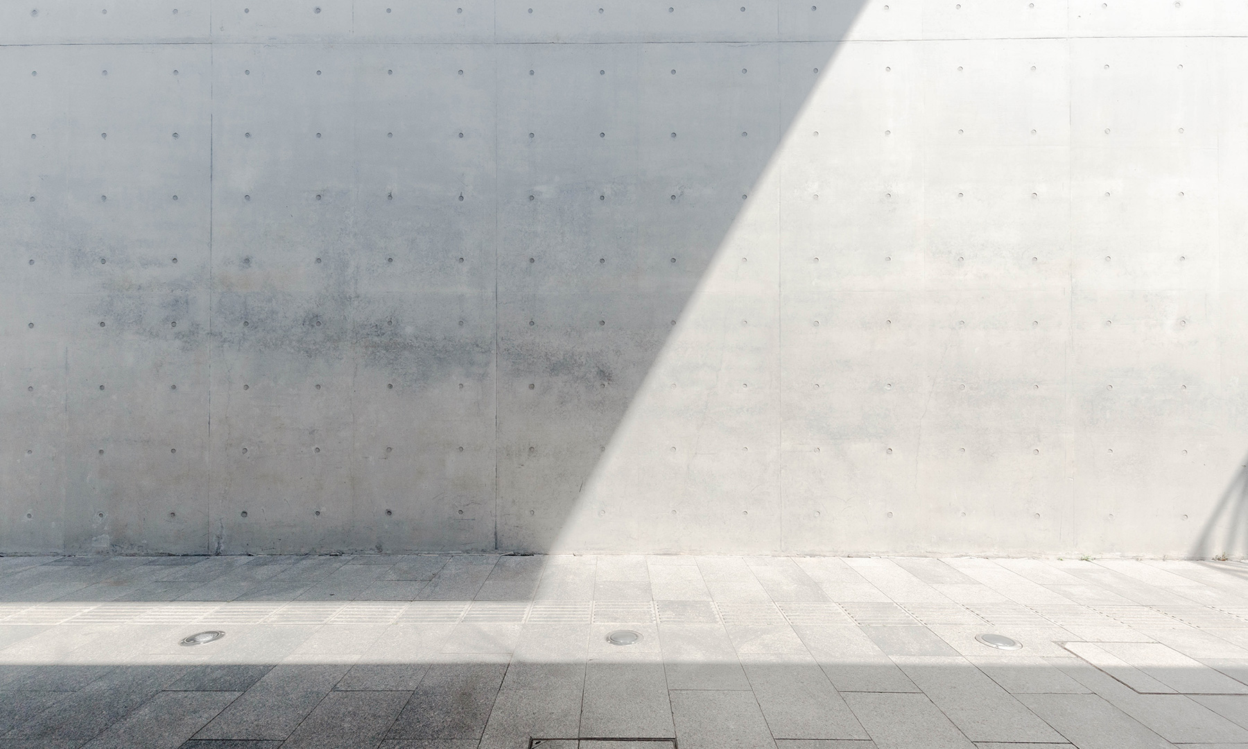 GFT Solution: Performance Optimization Clean concrete wall with a sharp diagonal beam of sunlight creating a geometric shadow across a modern paved surface.