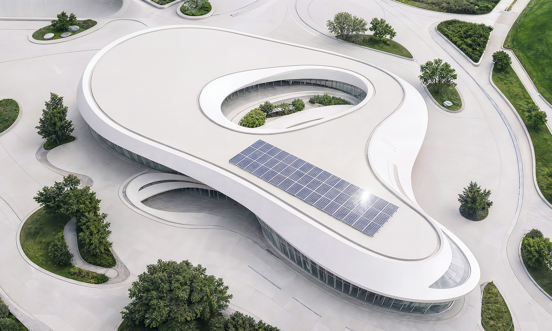 Vista aérea de um edifício moderno com painéis solares no telhado, cercado por áreas verdes ajardinadas e um projeto arquitetônico orgânico.