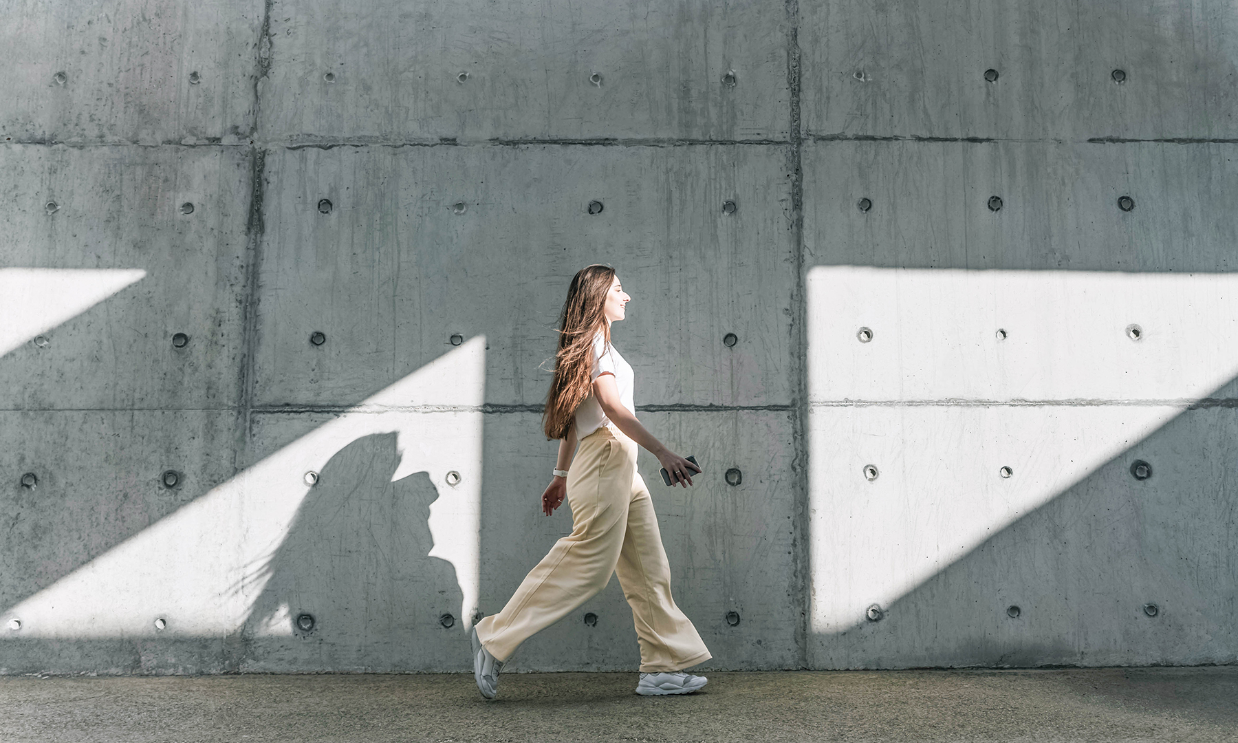 Person walking confidently beside a modern concrete wall with geometric shadows, symbolizing progress and purpose.