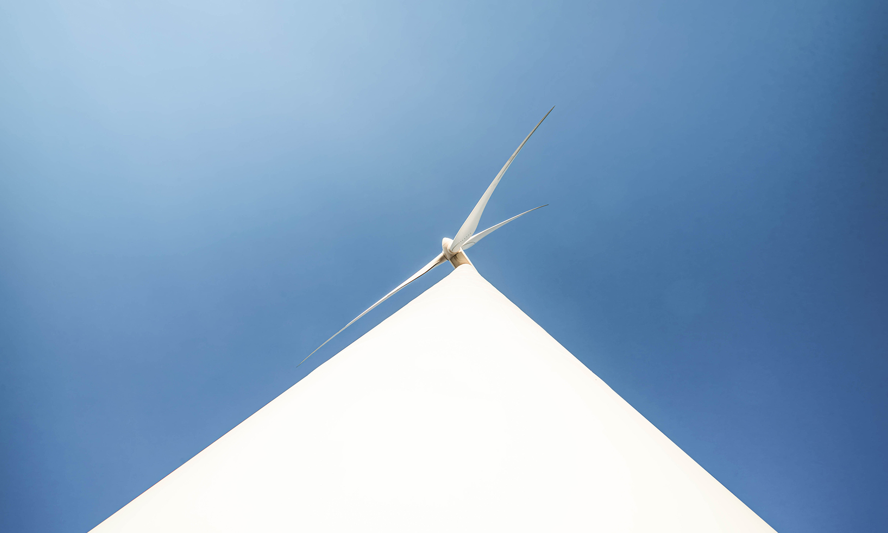 Wind Turbine Against Clear Blue Sky Upward view of a modern white wind turbine set against a clear blue sky, symbolizing renewable energy and clean technology.