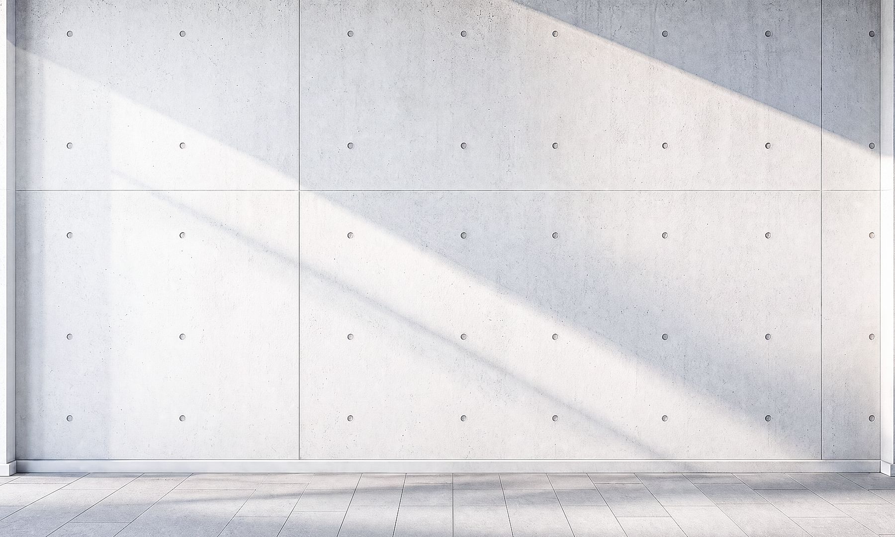 Minimalist concrete wall with geometric paneling and soft diagonal shadows created by natural light in a modern architectural space.