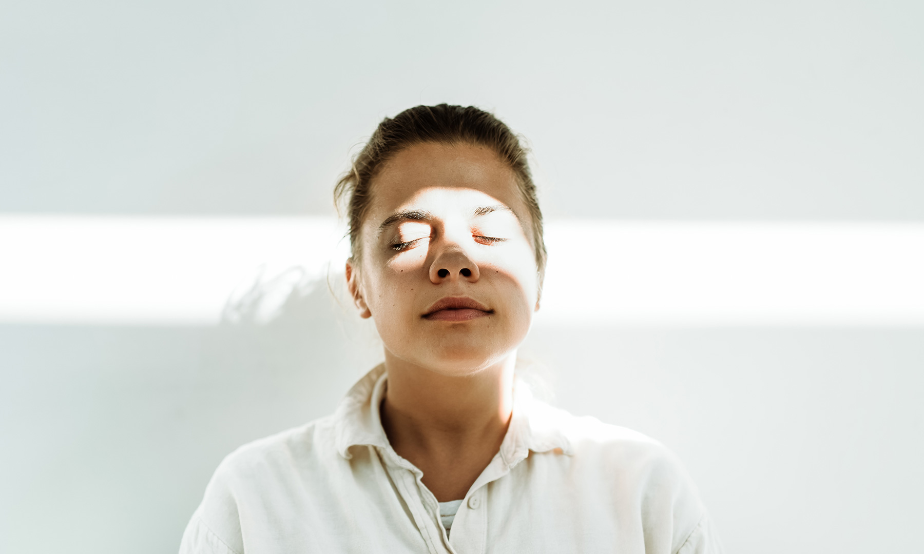 Person with closed eyes illuminated by a beam of light, symbolizing mindfulness, balance, and inner clarity.